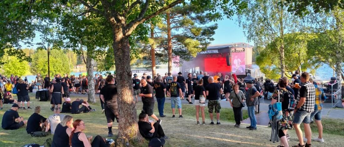 Ihmisjoukko ulkoilmassa John Smith -festareilla nurmikolla puiden alla.
